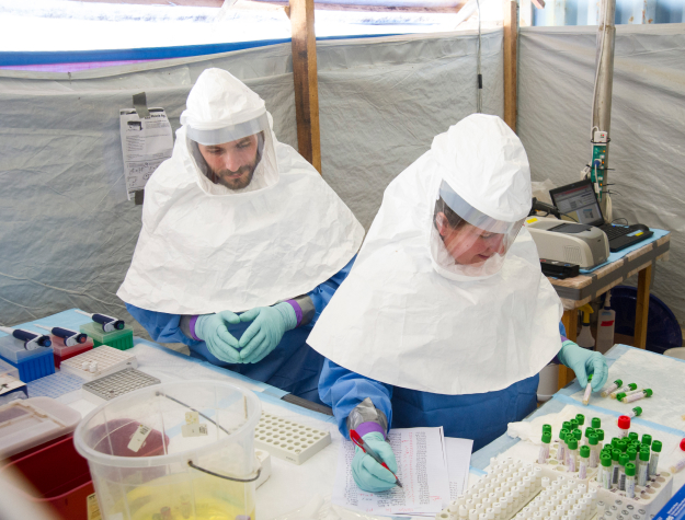 Two people wearing protective equipment in a tent lab examining samples