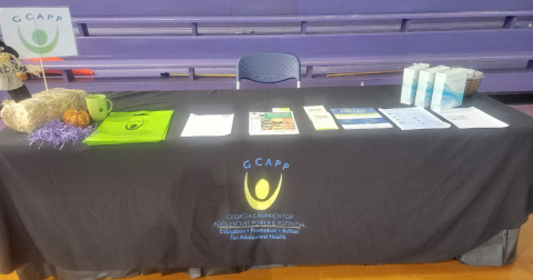 A table with black table cloth that says "GCAPP" has HIV self-testing papers and kits on it.