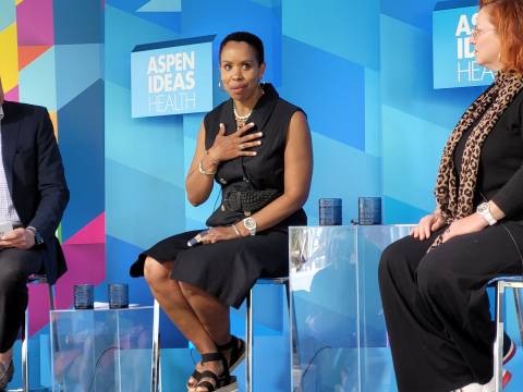 A black woman with short hair and a black dress speaks on a panel. 