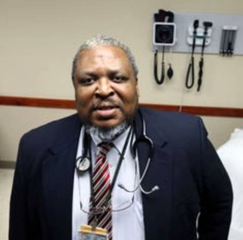 An black doctor in a suit with salt-and-pepper hair and beard