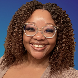 A black woman with curly brown hair smiles at the camera